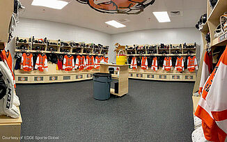 An empty locker room with REGUPOL aktiv Rolled Rubber Flooring and rows of lockers, filled with gear.