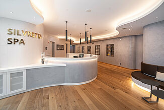 Reception with curved counter and wooden floor in the spa area of the Silvretta Therme in Ischgl.