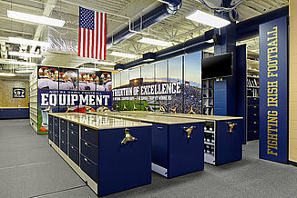 Notre Dame football equipment room with lockers, American flag, and gray REGUPOL aktiv flooring.