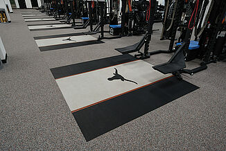 Angled view of rows of weight racks found at the University of Texas at Austin. Individual platforms are offered for each weight rack, featuring REGUPOL crash and aktivpro roll, with a customized team logo.