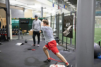 Athlete performs athletic training exercises while a coach supervises the athlete. The Kelowna High Performance facility features REGUPOL aktiv rolled rubber flooring. 