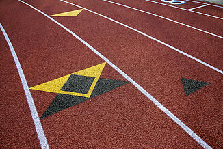 Black and yellow arrows are painted on a St. John's  REGUPOL champion AG running track, indicating the direction of running.