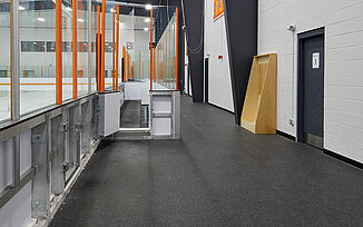 Walkway around the ice rink in the Thayer Sports Center. The walkway features REGUPOL aktiv rolled rubber flooring. Doorways throughout the walkway lead to locker rooms and offices throughout the facility.