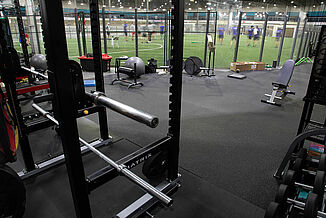 View of a weight rack and equipment at Kelowna High Performance, leading into the turf area of the facility. REGUPOL aktiv rolled rubber flooring is used throughout the non-turf areas of the complex.