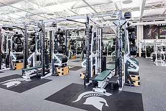 View of the weight racks that are available in the Michigan State football weight room facility. Each weight rack has an individual REGUPOL crash zone that allows for increased durability and features an inlaid Spartan logo.