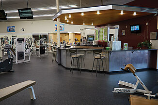 The reception center of New York Fitness, featuring REGUPOL aktiv rolled rubber flooring. The floor provides a seamless and non-slip option that promotes safety as members enter and exit the facility. Three members enjoy the amenities offered in the reception area.