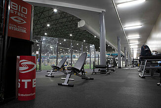 Two weight benches and various other athletic equipment sits on REGUPOL aktiv rolled rubber flooring in Kelowna High Performance. The REGUPOL flooring surrounds the turf area of the facility and provides a seamless flooring for weight training purposes.