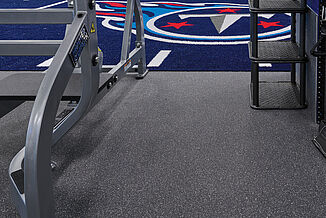 Tennessee Titans Practice Facility weight room with Thunder Gray REGUPOL aktivpro roll rubber flooring, featuring a blue, red, and white logo on a custom blue turf area. Hammer Strength lifting equipment can also be seen within the image.