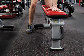 A weight bench rests atop REGUPOL aktiv rolled rubber flooring in the UFC Gym in Lancaster. The athlete utilizes the bench to perform weighted dumbbell rows. 