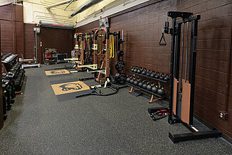 Full view of the weight training area of the Hershey Bears weight room, featuring two squat racks, cable machine and dumbbell rack.