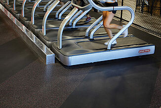 The front angled view of a row of treadmills resting on REGUPOL aktiv rolled rubber flooring in the UFC Gym located in Lancaster. An athlete is in motion on the treadmill.