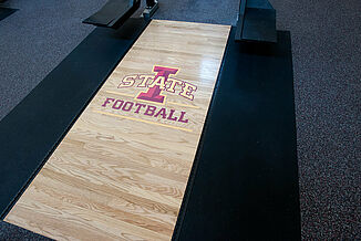 Angled view of the Iowa State platforms located within the athletic weight training facility. Each platform features REGUPOL crash and aktivpro roll flooring, along with an inlaid logo.