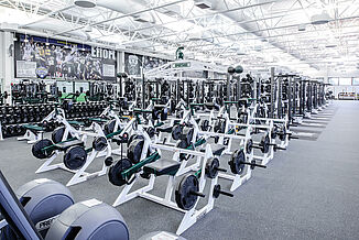 View of the number of different machine and equipment that are offered to athletes in the Michigan State football weight room. All equipment is positioned on REGUPOL aktivpro roll flooring in Thunder Gray.