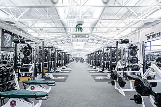 The length of the Michigan State football weight facility, showcasing the vast number of free weights, weight racks and machines throughout. All of the equipment rests on REGUPOL aktivpro roll flooring and REGUPOL crash.