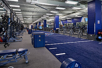 Tennessee Titans’ Practice Facility weight room, featuring various exercise equipment, including free weights, benches, machines and plyometric boxes, with Thunder gray REGUPOL aktivpro roll flooring with custom blue and red accents.