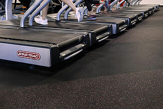 A row of treadmills sitting on REGUPOL aktiv rolled rubber flooring in the UFC Gym in Lancaster. An athlete exercises on the treadmill.