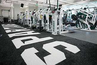 Spartans turf area located in Michigan State hockey weight room, seamlessly transitioning with REGUPOL aktivpro roll flooring. Fitnessn equipment is located throughout the room, allowing for a variety of different exercise options for athletes.