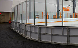 Indoor ice rink at Thayer Sports Center with white surface, orange lines, and glass walls, set in a large room with REGUPOL aktiv rubber rolled flooring and white walls.