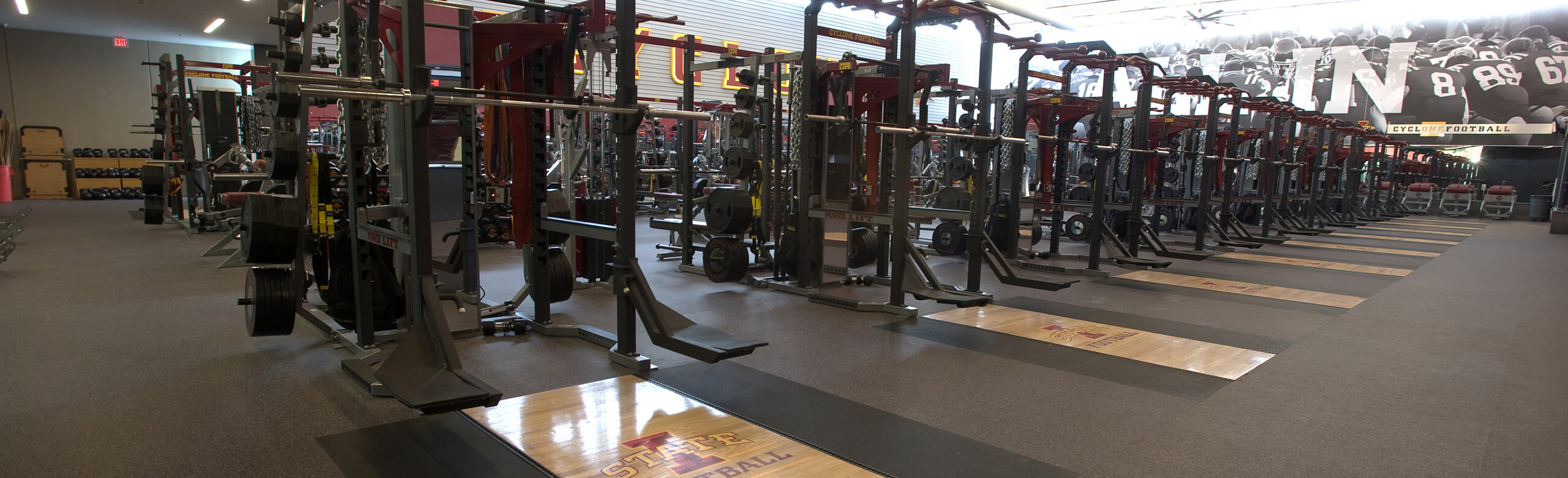 A row of weight training racks at Iowa State, each with individual platforms. REGUPOL aktivpro roll flooring and REGUPOL crash is featured throughout the facility.