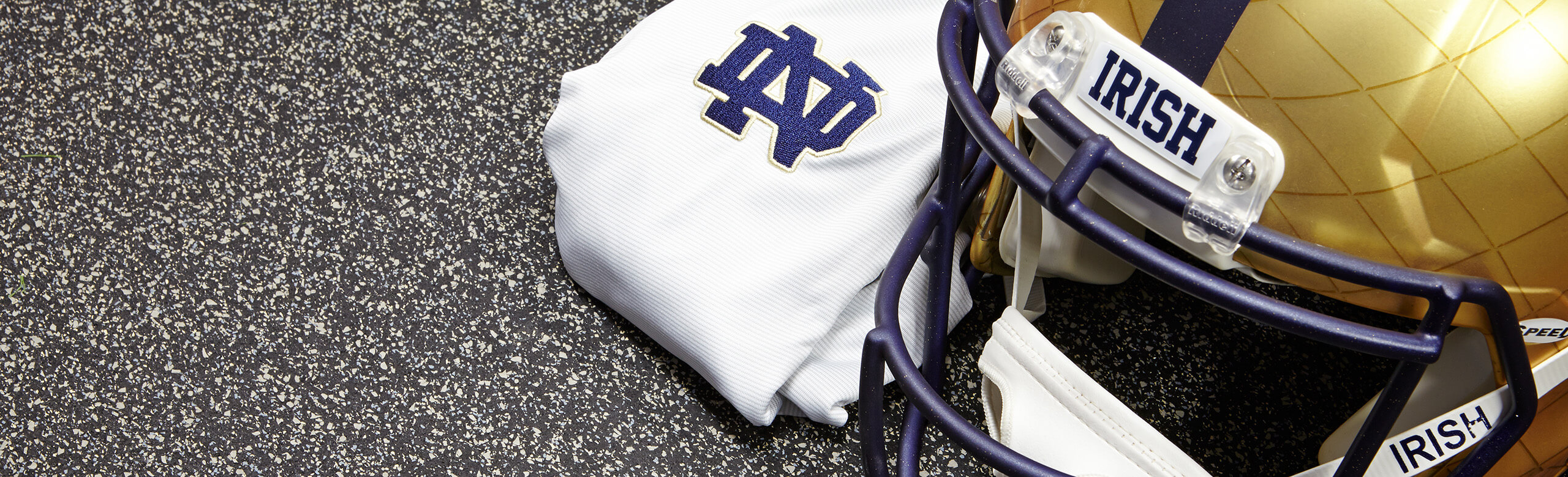 A gold Notre Dame helmet and a white cloth displaying the Notre Dame logo are arranged on REGUPOL aktiv floor.