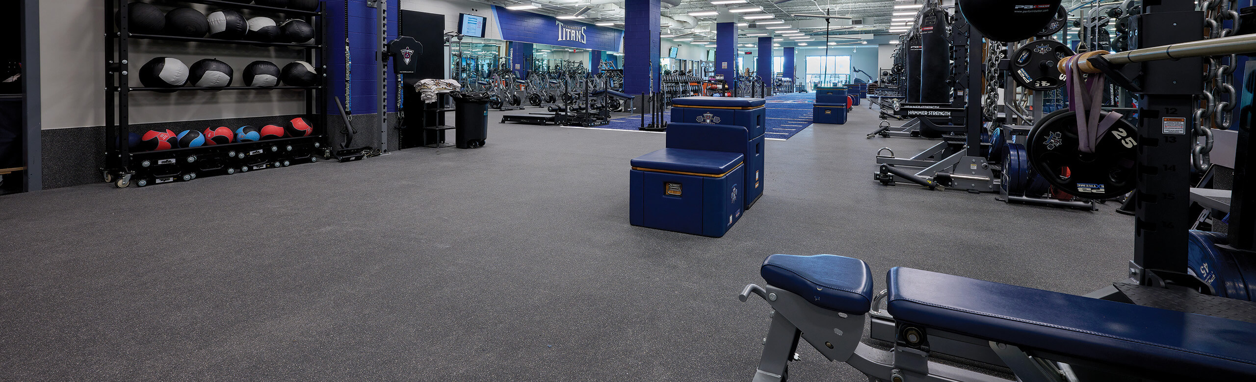 Weight room at Tennessee Titans practice facility with Thunder Gray REGUPOL aktivpro roll flooring, blue and black equipment, and various free weights and training tools.